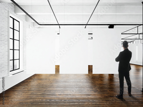 Businessman Modern art museum expo loft interior.Open space studio.Empty white canvas hanging.Wood floor,bricks wall,panoramic windows.Blank frames ready for bussiness information.Horizontal mockup.