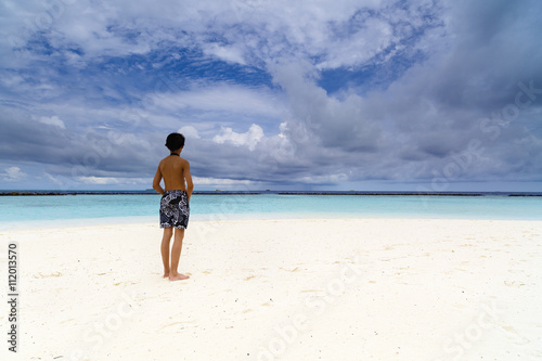 young boy sitting on exotic beach and watched the ocean