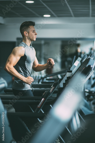 Canvas Print Young man in sportswear running on treadmill at gym