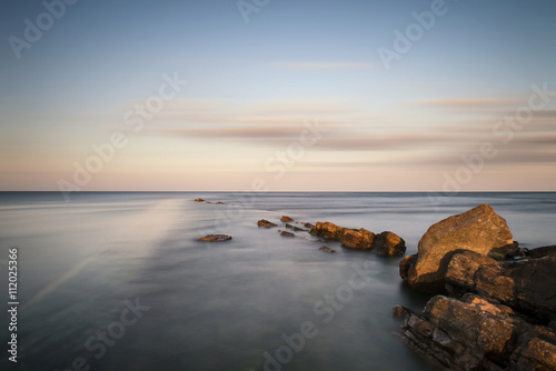 Stunning long exposure landscape of sea over rocks at sunset
