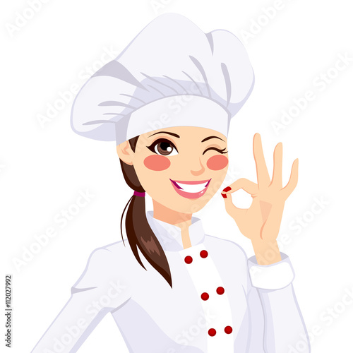 Young confident chef woman in uniform winking one eye and gesturing ok sign with her hand