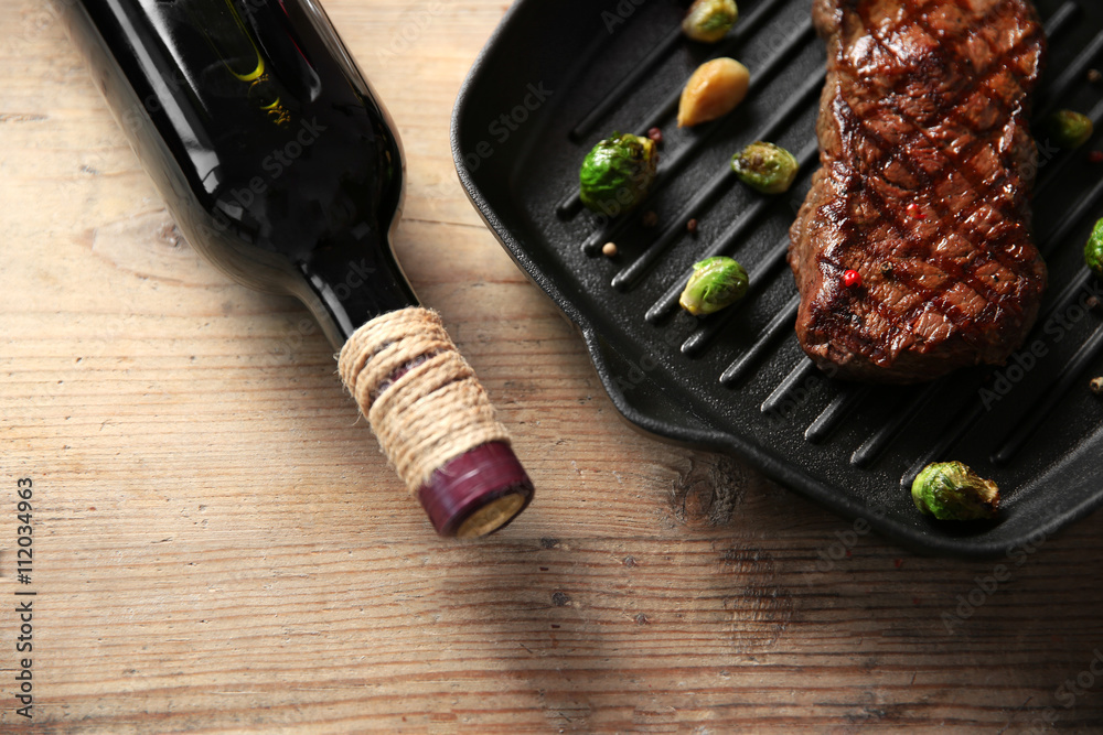 Obraz premium Grilled steak on grill pan with wine on wooden table