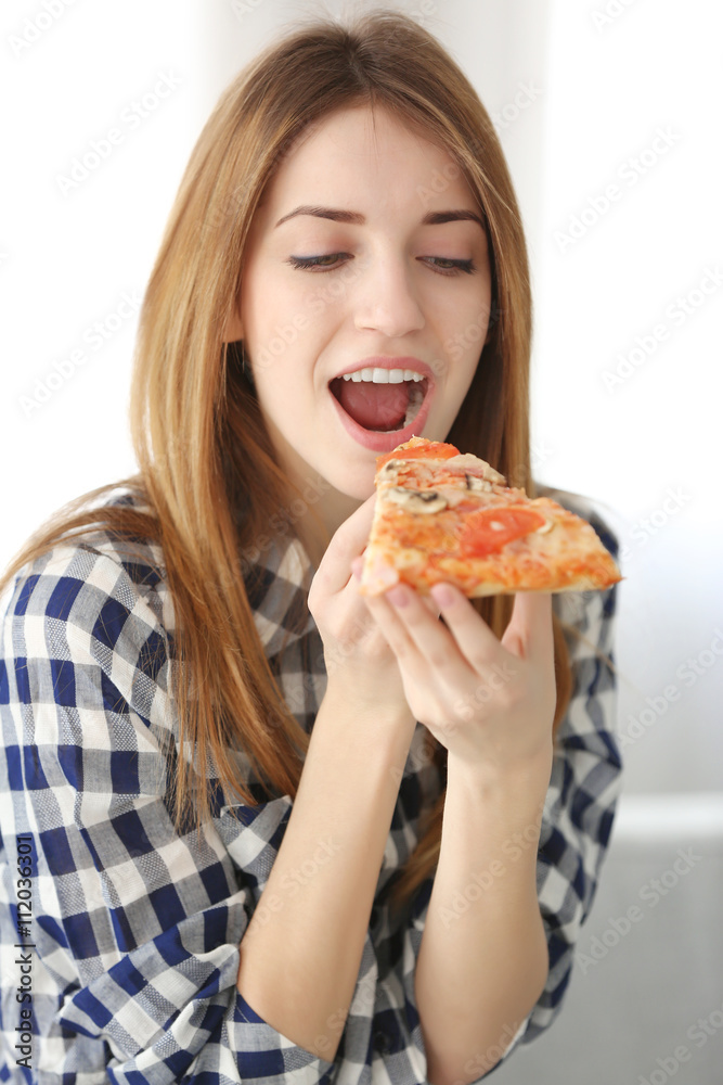 Happy young woman eating slice of hot pizza at home
