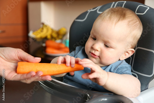 Female hand giving carrot to a baby in a chair