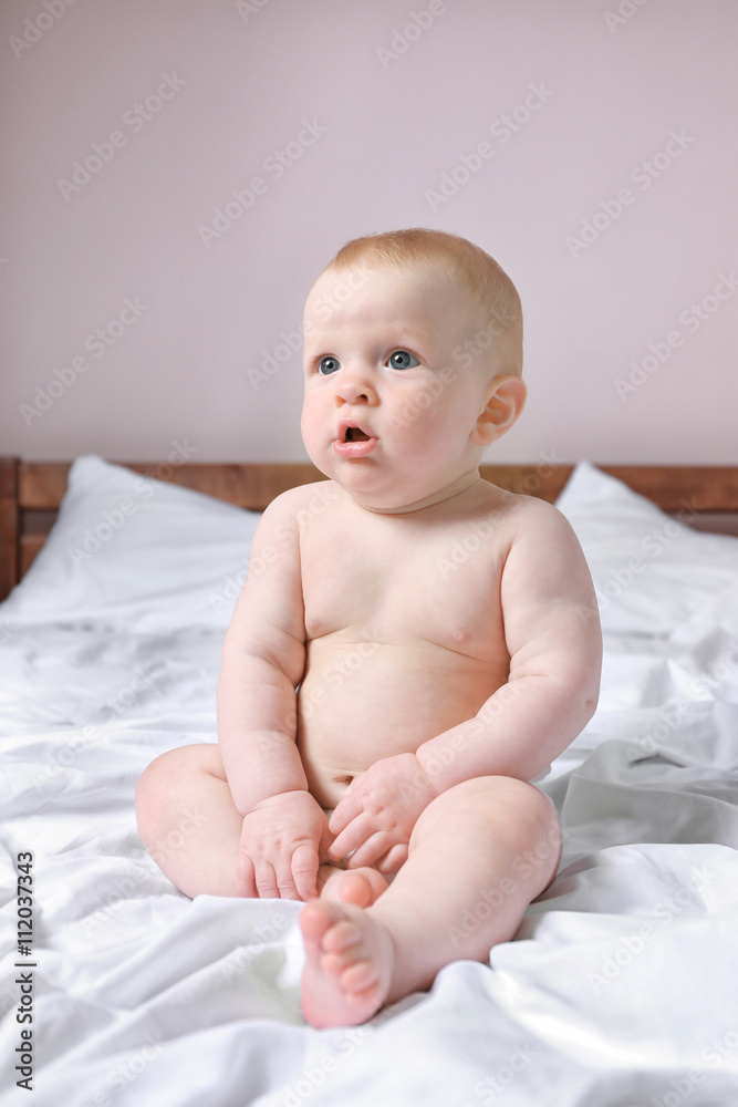 Adorable baby sitting on parents bed, close up Adorable baby sitting on parents bed, close up