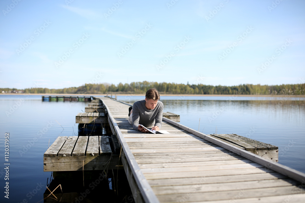 Young man on jetty reading book Young man on jetty reading book
