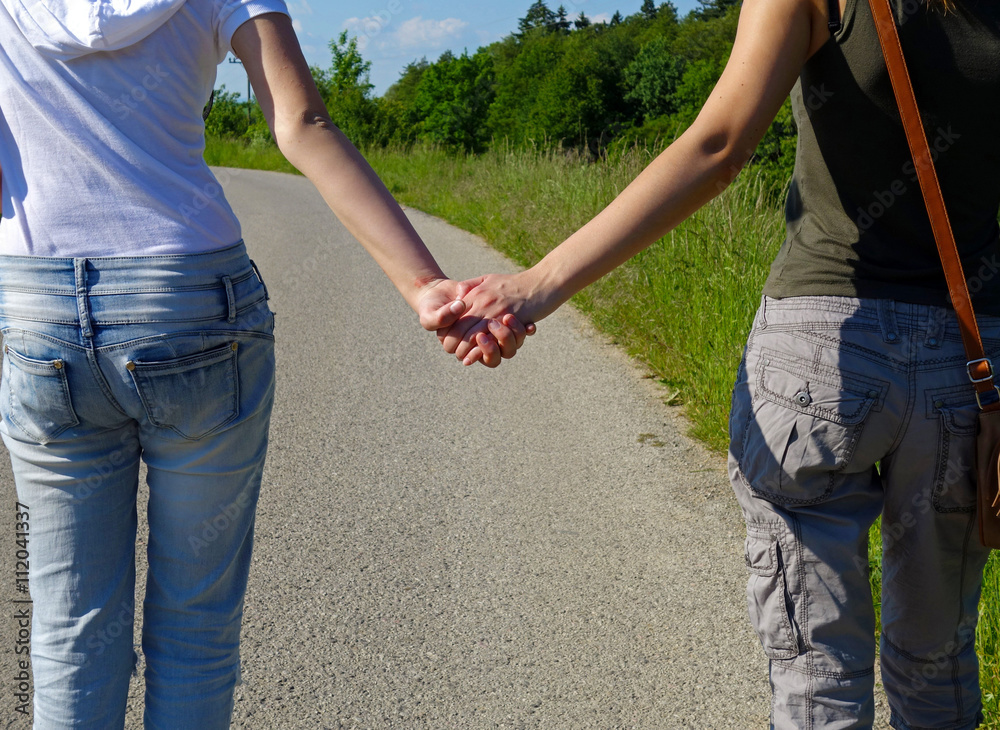 two young girls holding hands, walking on a road in the countryside two young girls holding hands, walking on a road in the countryside