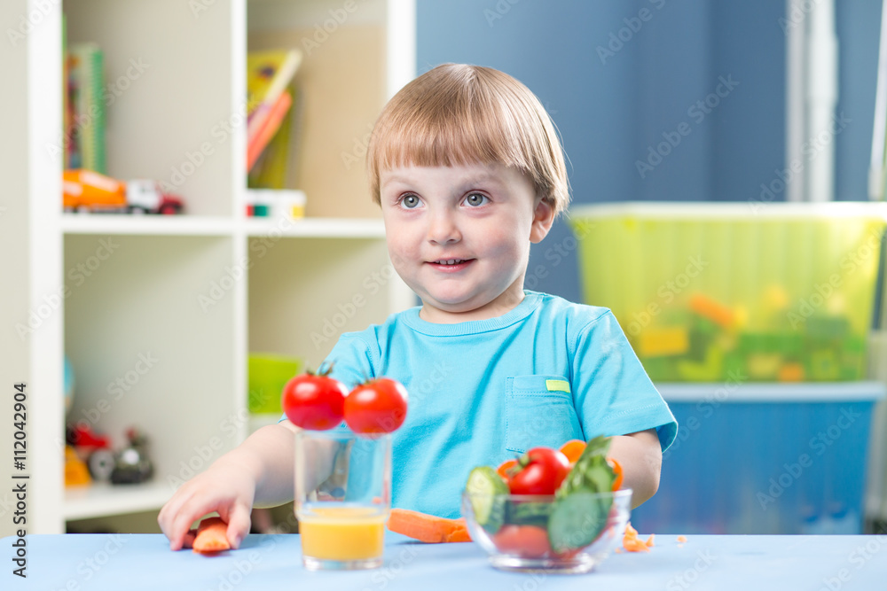 Cute little boy eats carrot and other vegetables in room