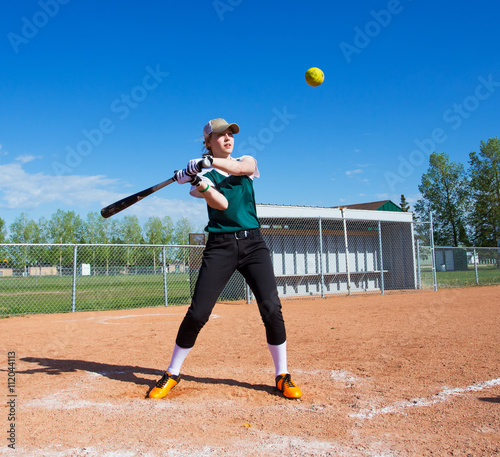 Photography A teenage girl wearing green and black baseball uniform standing at home plate o