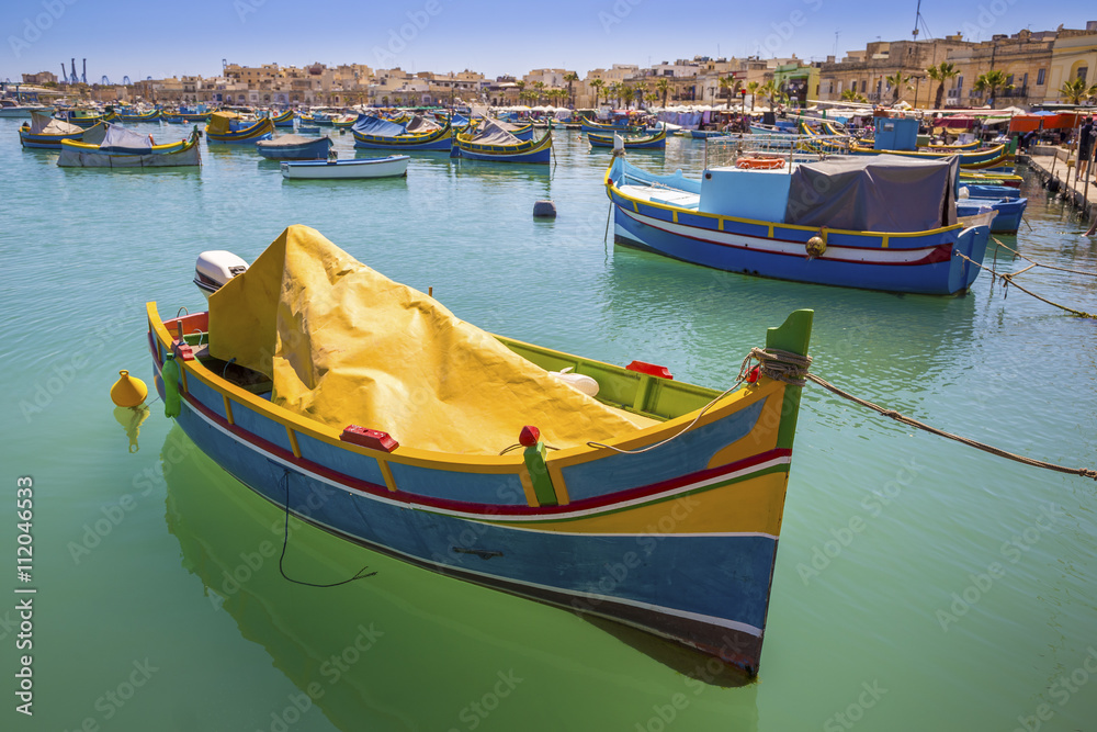 Malta - Traditional colorful Luzzu fishing boats at Marsaxlokk on a nice summer day with blue sky and crystal clear green sea