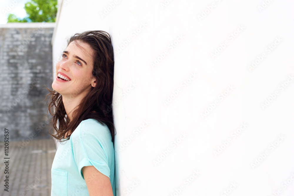 Smiling woman leaning against white wall looking up Smiling woman leaning against white wall looking up