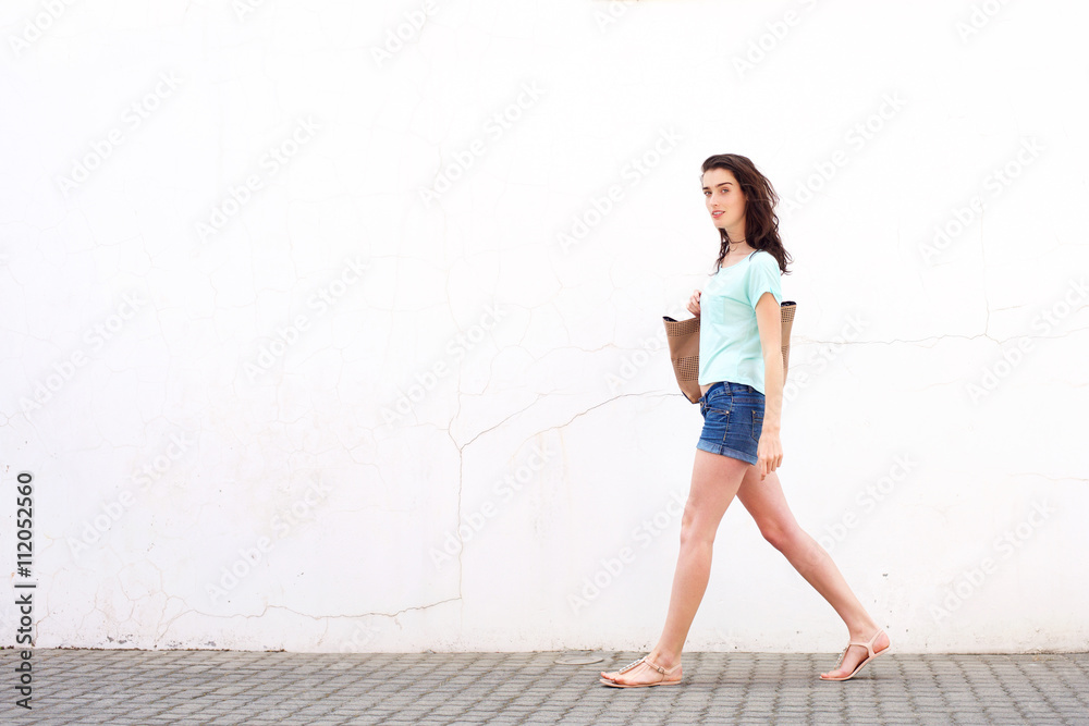 Smiling young woman with bag walking by white wall Smiling young woman with bag walking by white wall