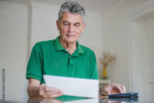 Senior man sitting at desk with paper and pocket calculator photo