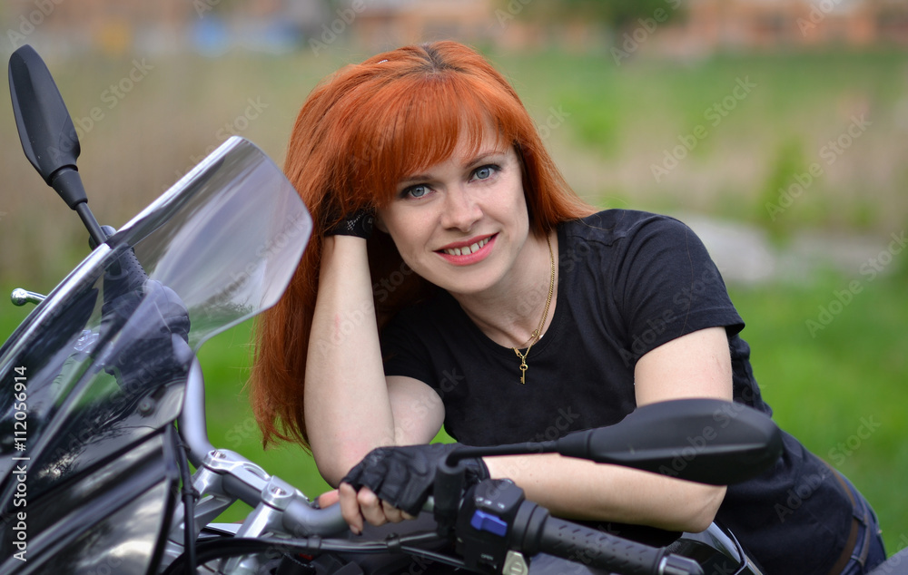 Interesting,cheerful,smiling,pretty,nice,good,friendly,lovely,adorable,redhead,red-haired professional biker girl with black,fast motorcycle,motorbike,bike,cute smile.Girl with motorbike,fast rider.