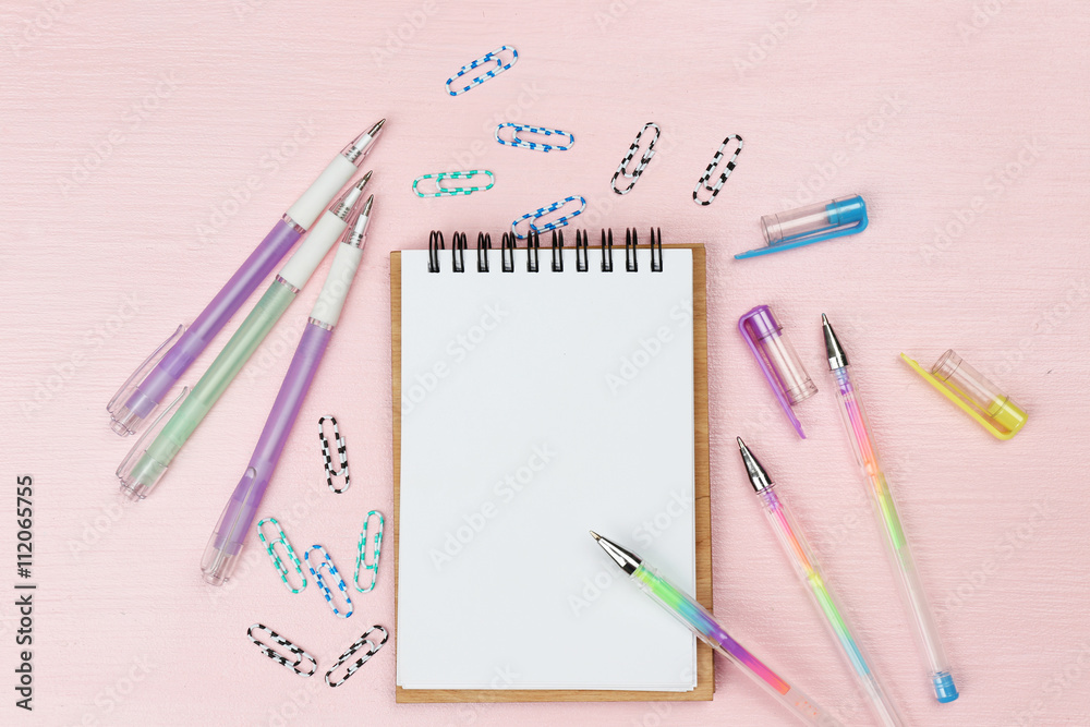 Office set with notebook, colored pens and clips on pink background Office set with notebook, colored pens and clips on pink background