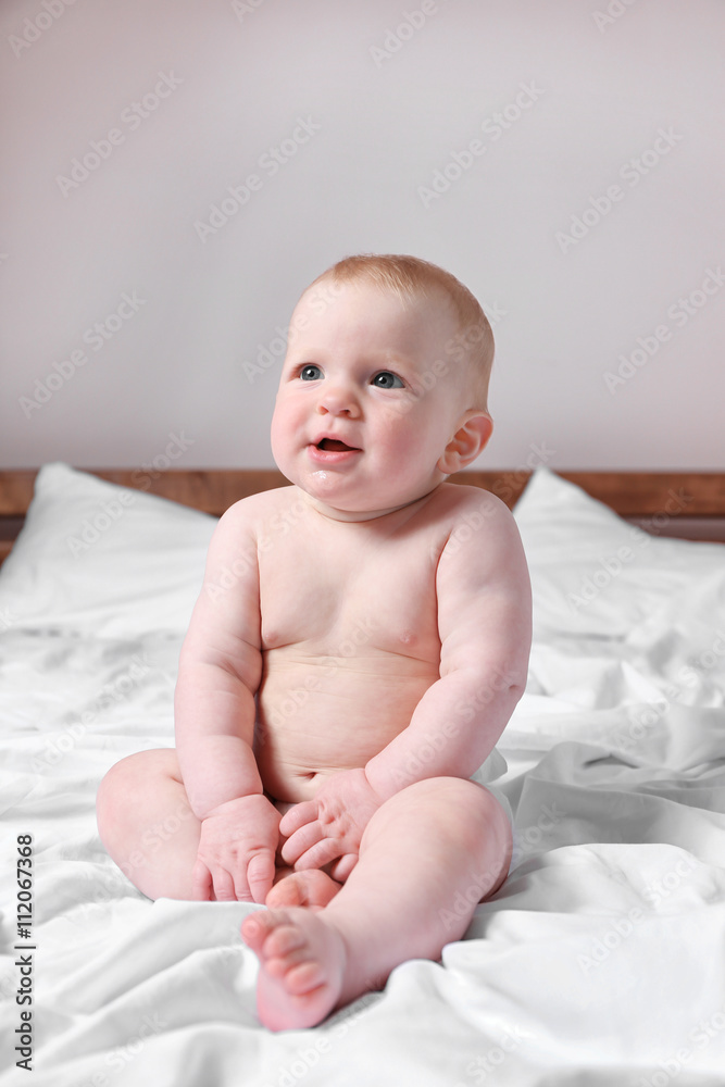 Adorable baby sitting on parents bed, close up Adorable baby sitting on parents bed, close up
