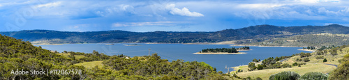 Lake Jindabyne landscape with a blue overcast sky and green rural foreground.  Featuring a number of islands including the two largest -  'Lion Island' and part of 'Cub Island'.