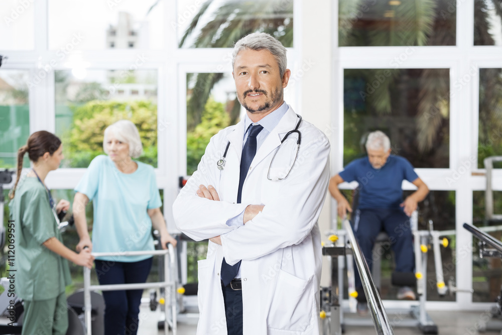 Confident Male Physiotherapist Standing Arms Crossed In Rehab Ce Confident Male Physiotherapist Standing Arms Crossed In Rehab Ce
