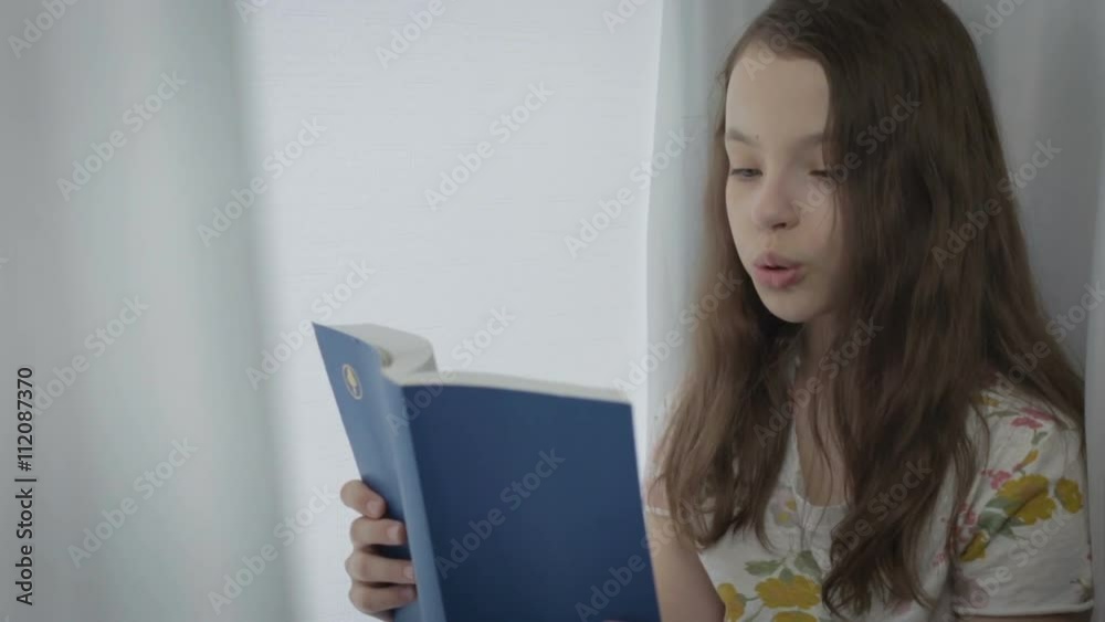 Beautiful little girl reading an interesting book by window. Beautiful little girl reading an interesting book by window.