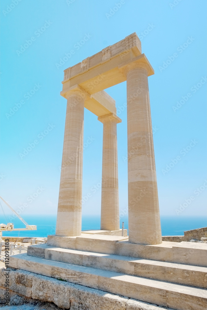 Famous Greek temple three pillars against clear blue sky and sea in Lindos Acropolis Rhodes Athena Temple, Greece