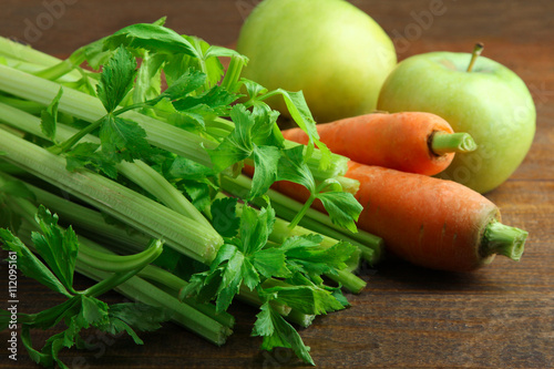 Fresh green celery with carrots and apples on a brown wooden background