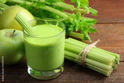 Fresh green celery juice in glass near green Apple on the brown wooden background