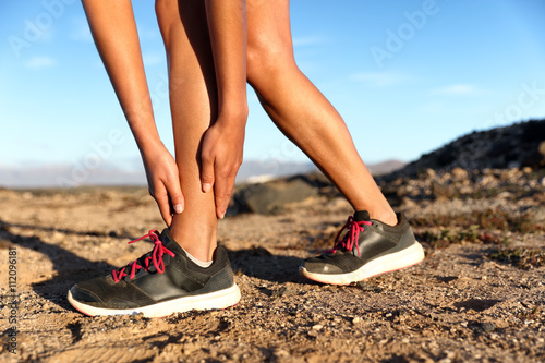 Runner woman with hurt ankles in pain during marathon. Athlete woman running outside with body injury. Sprained ankle on trail run in summer outdoors nature. Fitness leg accident on cardio workout.