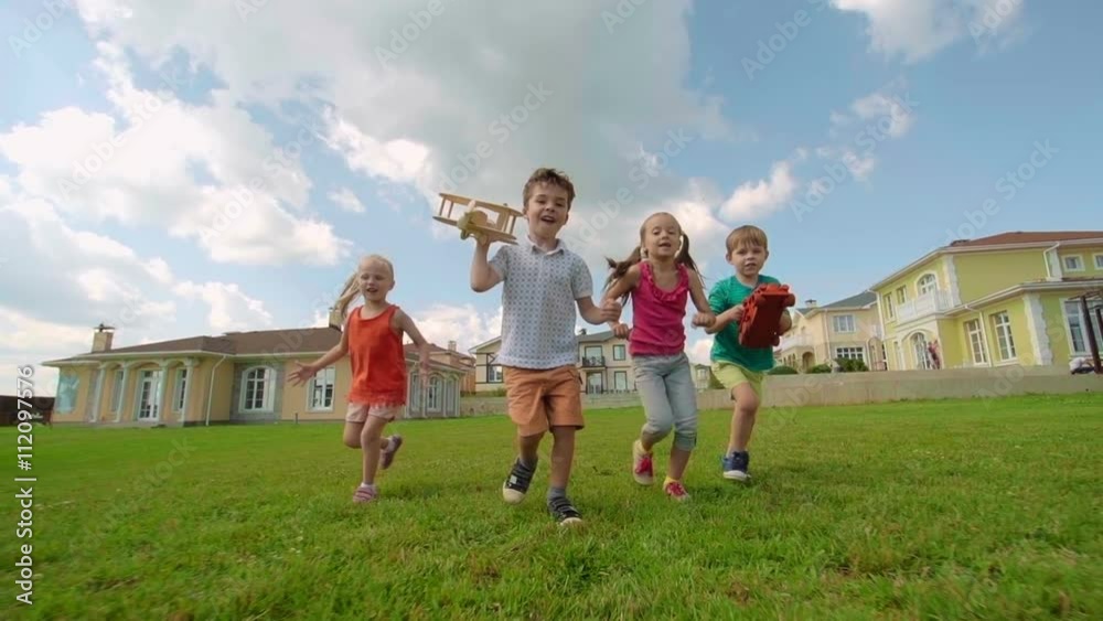 Two little boys and girls running on green grass together in slow motion Two little boys and girls running on green grass together in slow motion