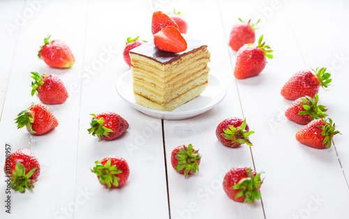 Beautiful delicious homemade cake with strawberries on white wooden table.
