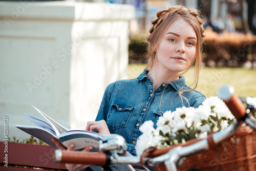 Beautiful woman with bicycle reading magazine on the bench outdoors