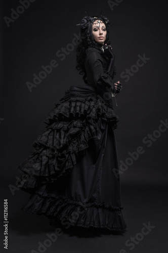 Fatal woman in vintage black dress posing on dark background