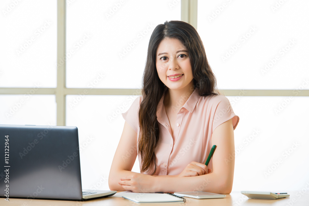 Successful Asian female entrepreneur sitting and smiling at desk Successful Asian female entrepreneur sitting and smiling at desk