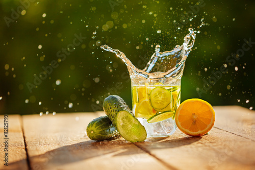 Detox water with lemon and cucumbers with splash on wooden table photo