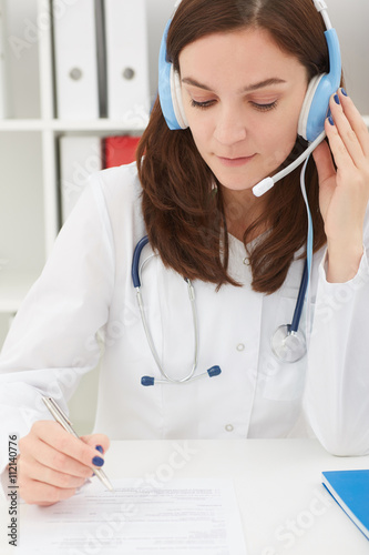 Obraz na płótnie Portrait of a beautiful medical secretary with handset at hospital. She write at medical form. Medical cure and tests advertisement concept. w salonie