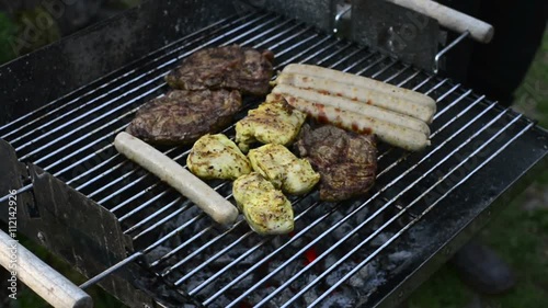 person tending different kinds of meat and sausages on a barbecue grill
