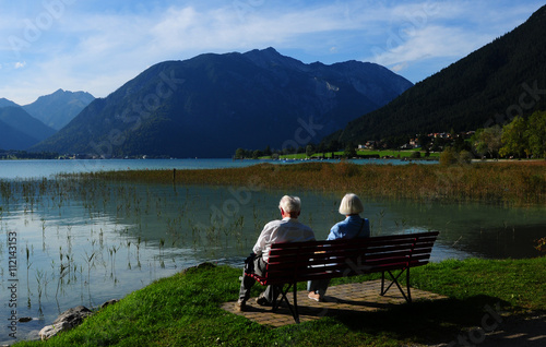 Ein älteres Paar sitz auf einer Bank am Ufer des Achensee's im Tirol. 
