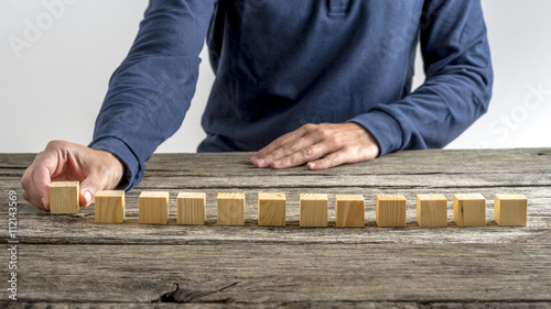 Front view of a man placing 12 blank wooden cubes in a row