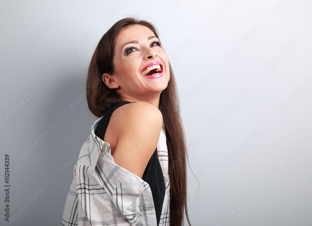 Happy casual toothy laughing woman looking up on blue background Happy casual toothy laughing woman looking up on blue background
