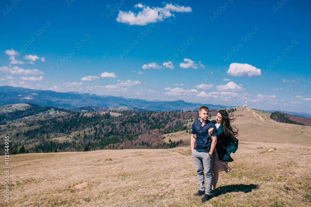 beautiful couple tender girl in a green dress and a guy in a bles shirt against the sky in a mountainous place