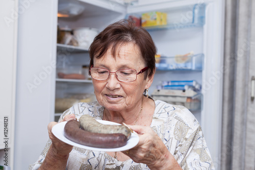 Happy senior woman holding plate with pork liver sausages