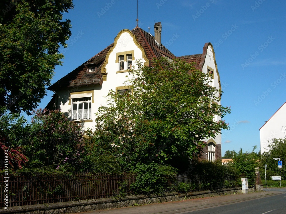 Weiße Gründerzeit Villa vor azurblauem Himmel mit üppigem grünen Garten