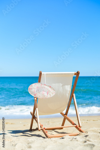 Back View Of Woman's Hat and Deckchair On Sandy Beach