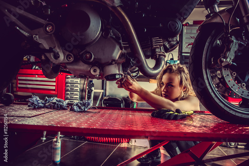 Blond woman repairing motorcycle.