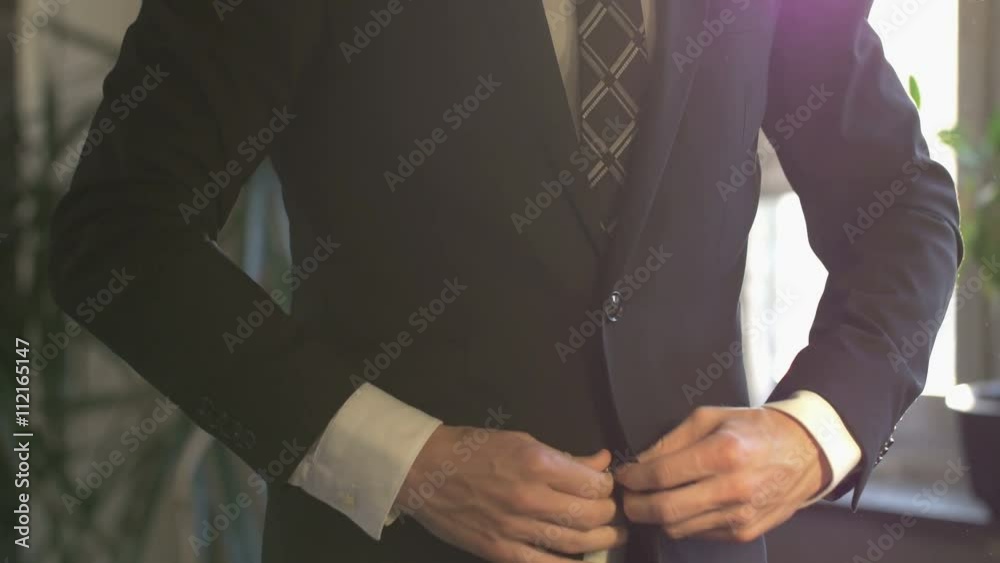 Elegant business man in white shirt correcting his tie and buttoning his suit jacket. close up