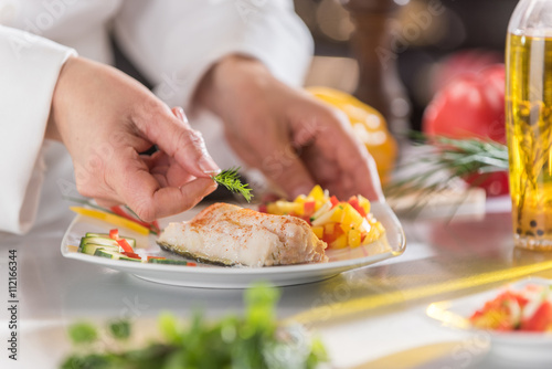 Fototapeta Naklejka Na Ścianę i Meble -  Hands of a chef putting the finishing touches on his fish dish