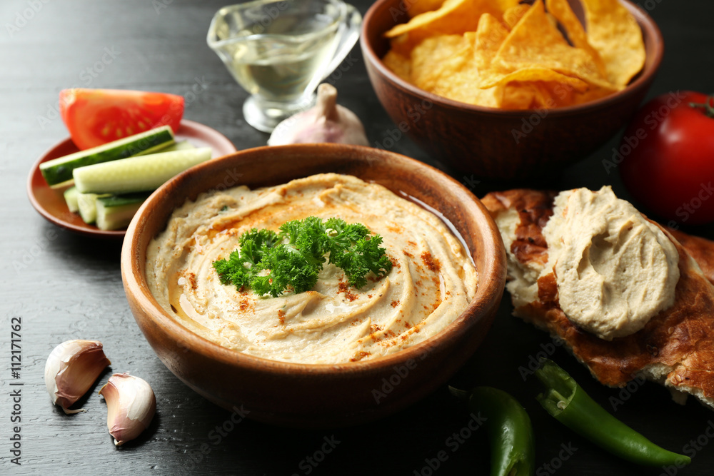 Wooden bowl of tasty hummus with chips and parsley on table Wooden bowl of tasty hummus with chips and parsley on table