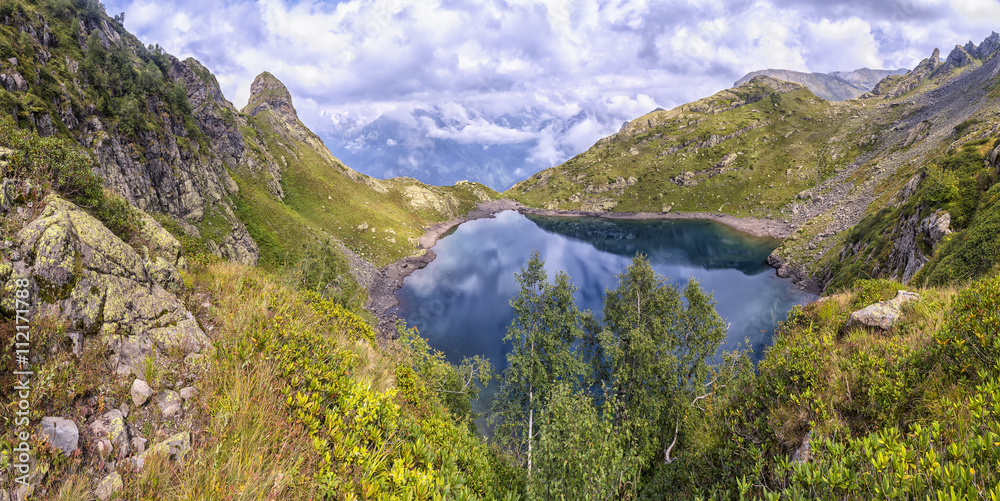 panorama landscape with clear lake in the mountains, huge rocks and Alpika and reflection of white clouds in Abkhazia in the Caucasus.