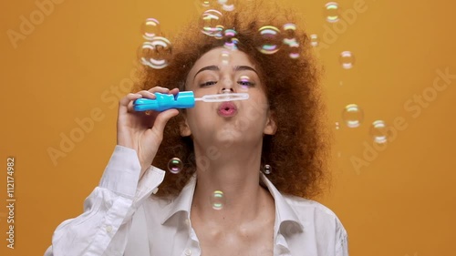 Funny fashion girl blowing soap bubbles on orange background. Close up. Slow motion