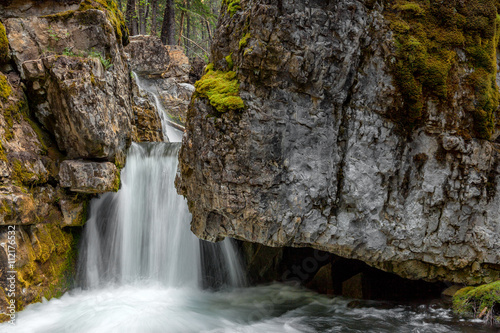 A small waterfall and stream flowing over the rocks through the forest in Kananaskis, Alberta Canada