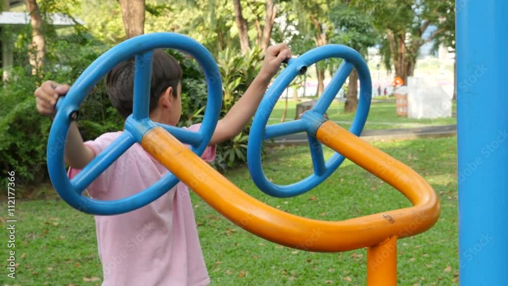 Asian kid boy exercise with wheel equipment at outdoor fitness in public park Asian kid boy exercise with wheel equipment at outdoor fitness in public park